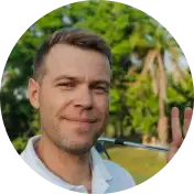Man smiling outdoors with trees in the background.